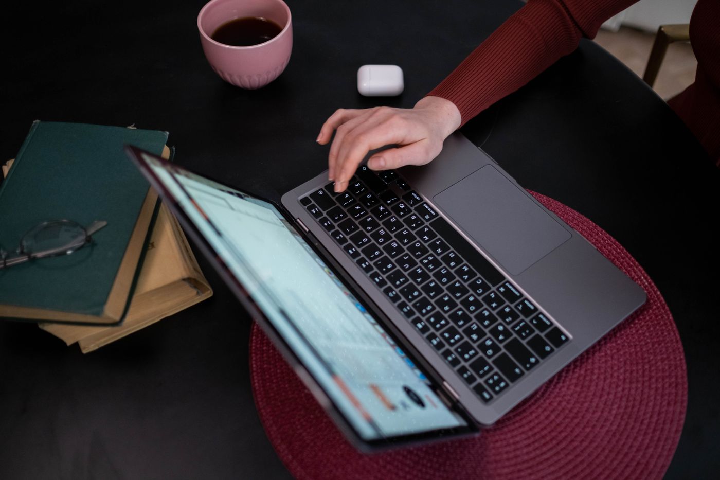 A person typing on a laptop at a desk with coffee and books